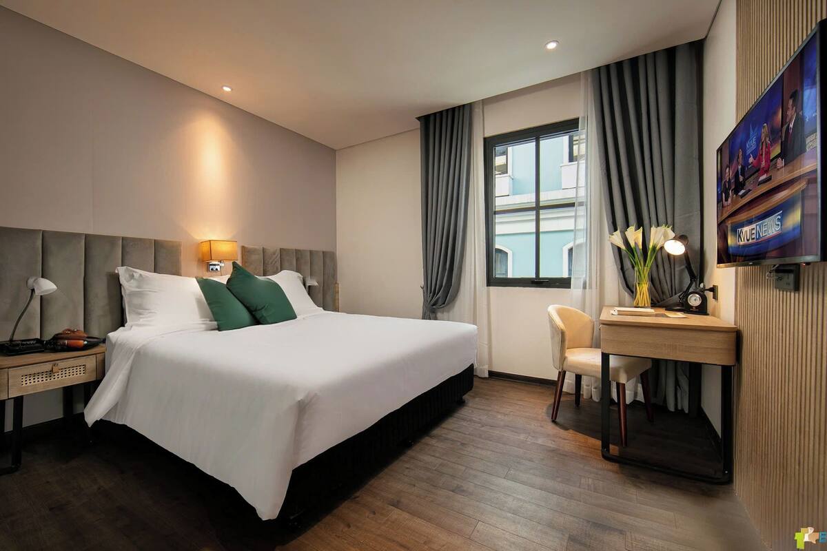 A hotel room with a bed, bedside table, lamp, chair, desk, and a TV mounted on the wall.