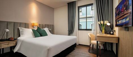 A hotel room with a bed, bedside table, lamp, chair, desk, and a TV mounted on the wall.