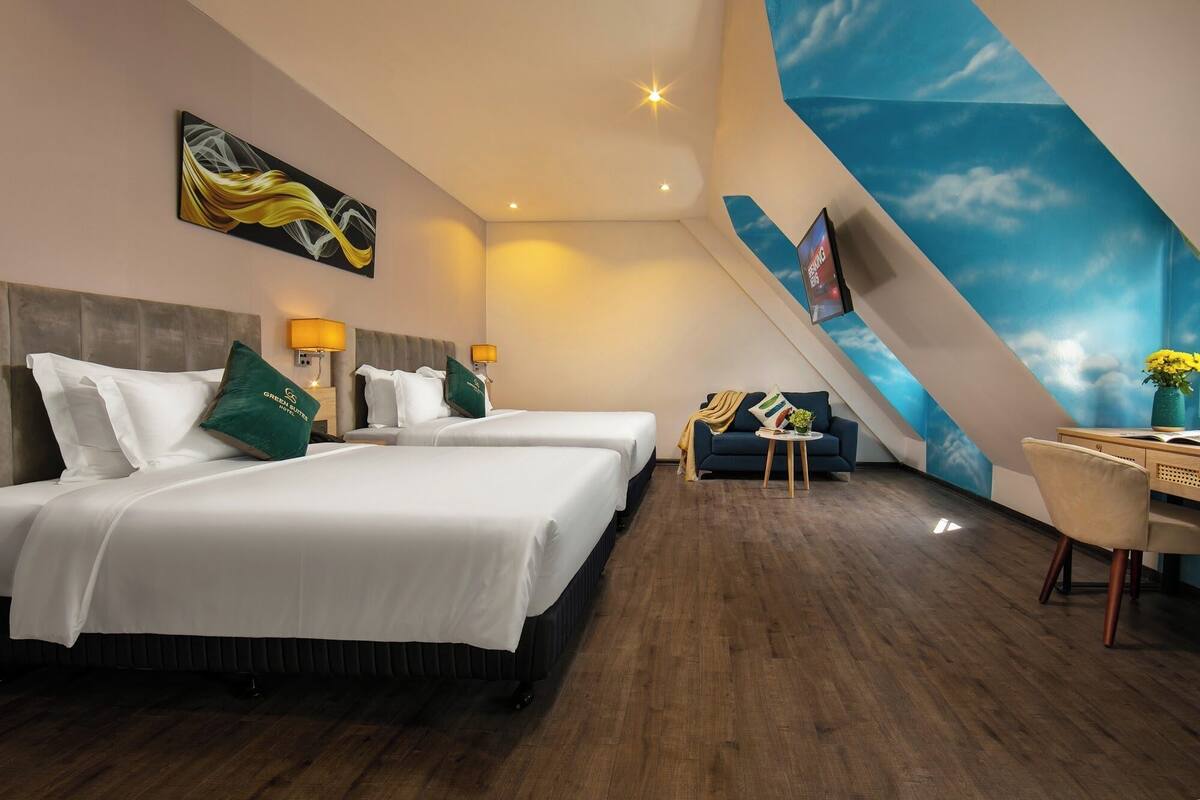 A hotel room with two beds, a desk, a chair, and a large window with a view of the sky.