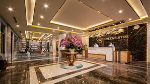 A hotel reception area with a marble floor, reception desk, and a large floral arrangement. - Green Suites Hotel Ha Long (Bai Chay)