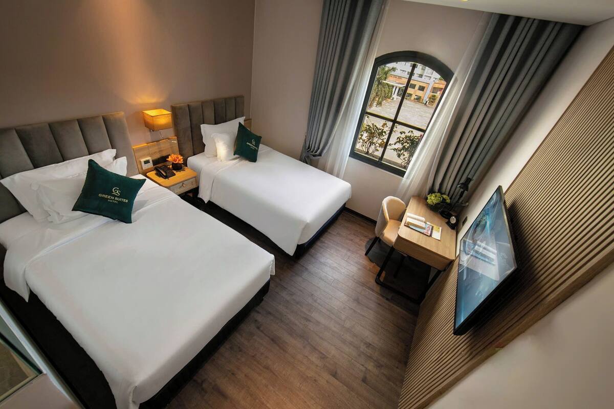 A hotel room with two beds, a desk, a TV, and a window with curtains.