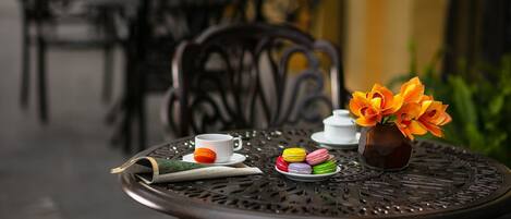 Una mesa metálica redonda con un periódico, una taza, macarons y un jarrón con flores.