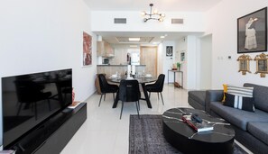 A modern living room with a flat-screen TV, a sofa, a coffee table, and a dining area with a table and chairs. - Premium 2BR Apt w/ Marina Views (Dubai)