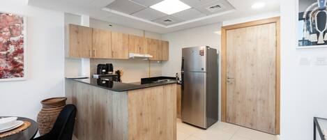 A modern kitchen with wooden cabinets, a stainless steel refrigerator, and a coffee machine.