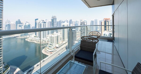 Un balcon situé dans un immeuble de grande hauteur, offrant une vue sur les toits d’une ville et sur une étendue d’eau.