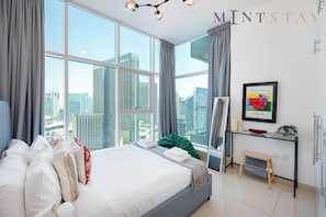 A modern hotel room with a large bed, a desk, and a view of tall buildings. - Premium 2BR Apt w/ Marina Views (Dubai)