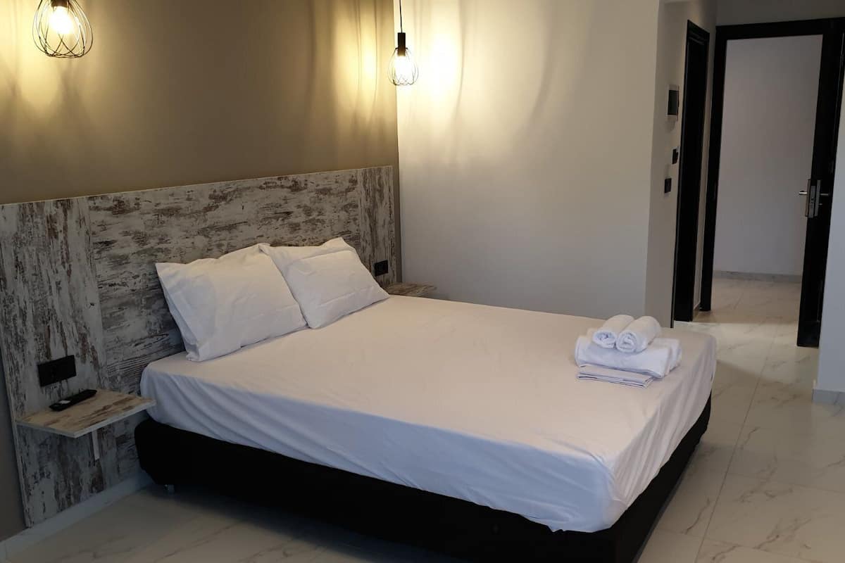 Una cama bien hecha con sábanas y toallas blancas, un cabecero de madera rústica y dos lámparas de pared.