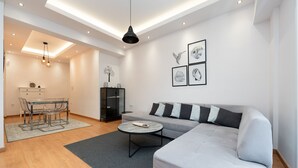A modern living room with a grey sofa, a round coffee table, and a dining area with a glass table and chairs. - Modern Family Apartment near Acropolis (Athens)