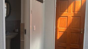 A hallway with a wooden door, a white wall, and a tiled floor.