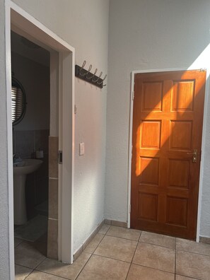 Un pasillo con una puerta de madera, una pared blanca y un piso de baldosas.