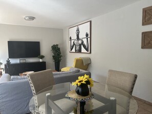 Una sala moderna con un televisor de pantalla plana, un sofá, una mesa de comedor con sillas y una obra de arte grande en la pared.