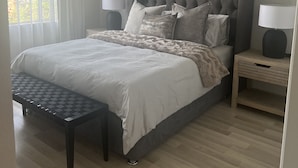 A bedroom with a large bed, two bedside tables with lamps, a bench, and a window with curtains. - Roodepoort Smart Home 1 (Roodepoort)