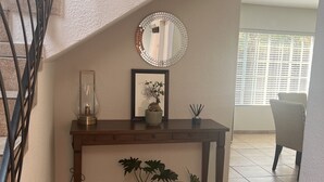 A staircase with a wooden handrail and a wall-mounted mirror. Below the mirror, there is a wooden console table with a vase, a framed picture, and a potted plant. - Roodepoort Smart Home 1 (Roodepoort)
