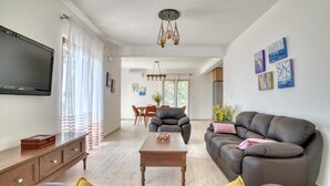 A modern living room with a sofa, a coffee table, and a TV. There is a dining area in the background with a table and chairs. - Seaview Villa Lavanda with pool (Drobnici)