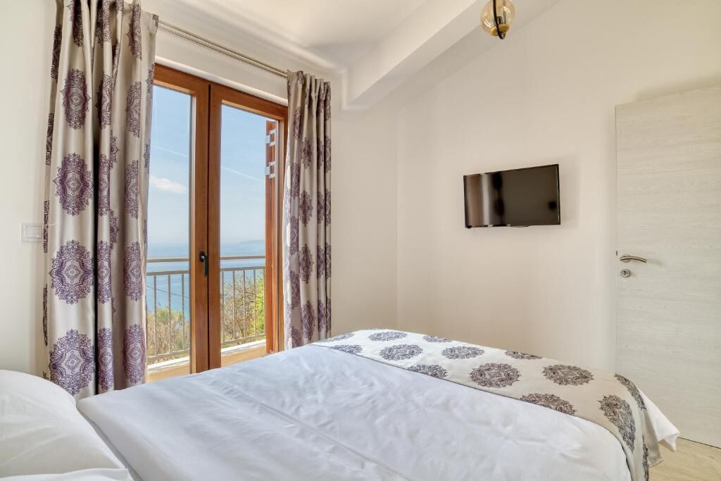 A bedroom with a bed, a TV mounted on the wall, and a balcony with curtains.
