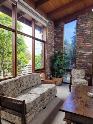 A cozy room with a wooden ceiling, large windows, a brick wall, a sofa, a chair, and a table. - Cosy house in a quiet area of Torquay (Torquay)