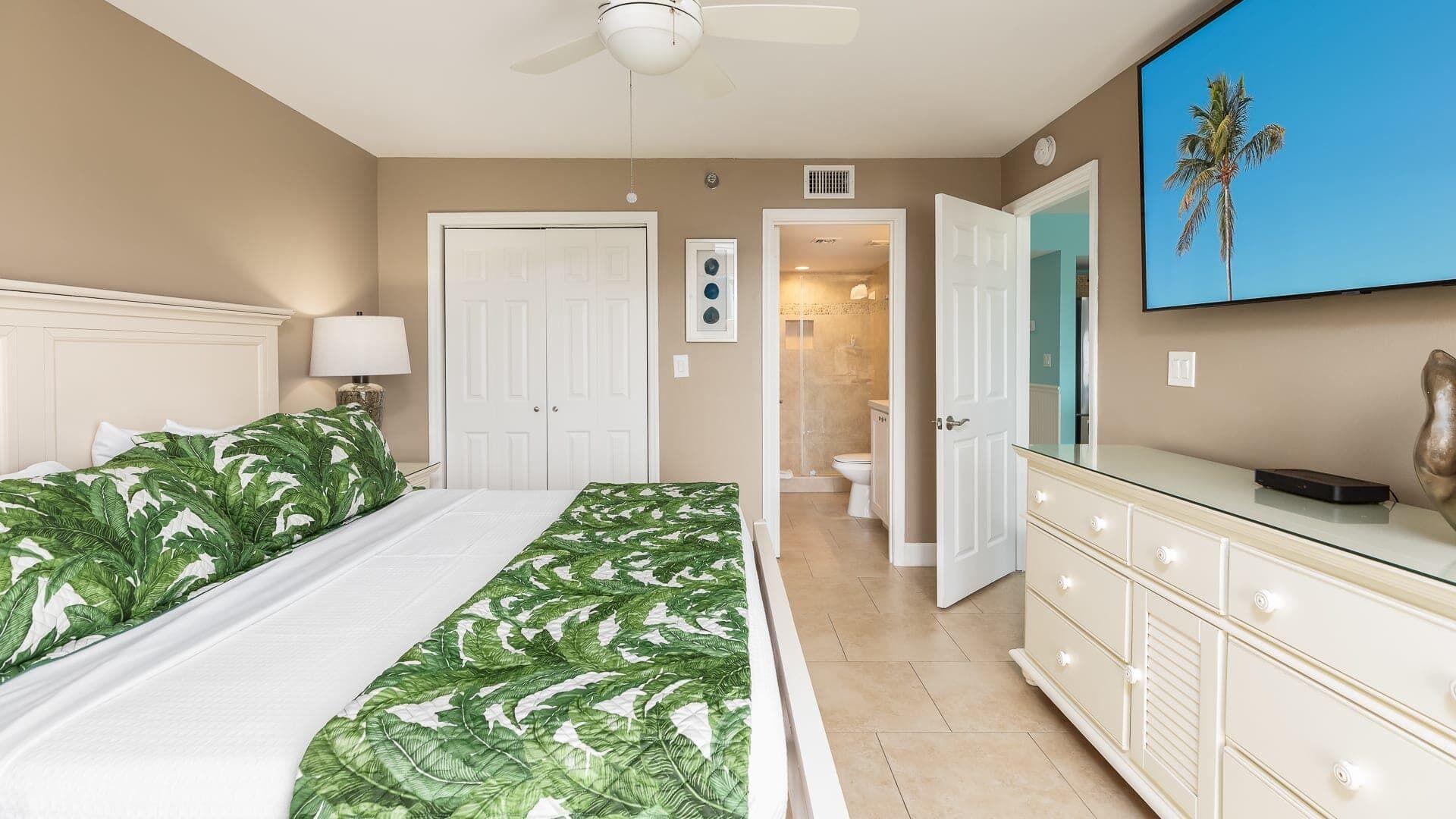 A bedroom with two beds, a bathroom, a vanity with drawers, and a ceiling fan.