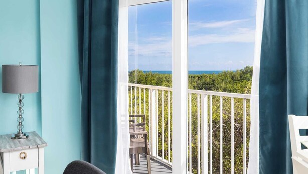 A balcony with a view of the sea, a chair, and a table with a lamp. - Boho Chic Ocean Pointe 3214 King & Queen (Tavernier)