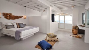 Un dormitorio moderno con una cama grande, una lámpara colgante y vista al mar a través de una puerta de vidrio.