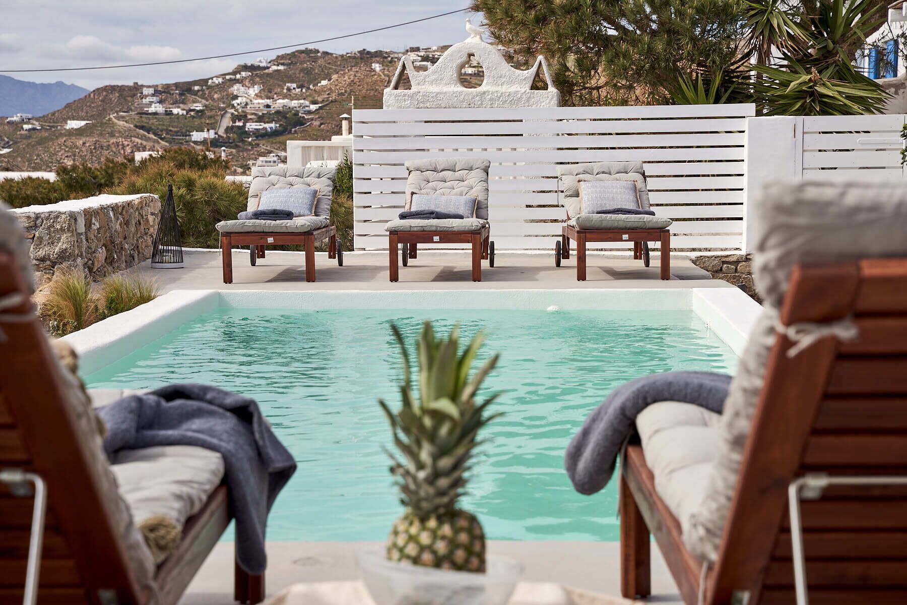 A poolside area with lounge chairs and a view of a coastal village.