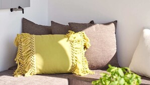Un salón moderno con un sofá, cojines, un colgante de macramé y una planta en maceta.