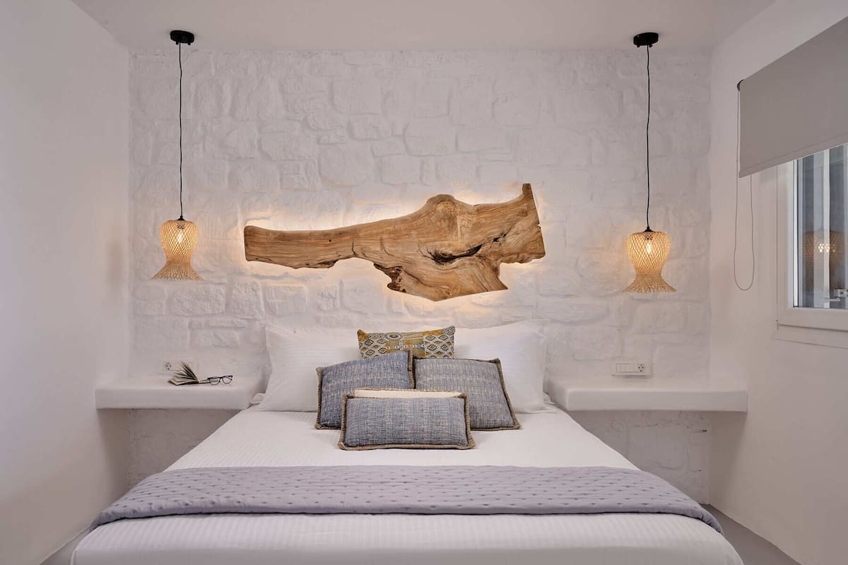 A bedroom with a white brick wall, a large wooden sculpture, and two pendant lights.