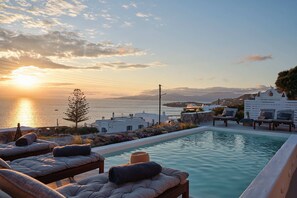 Ein Poolbereich mit Liegestühlen und Blick auf das Meer bei Sonnenuntergang.
