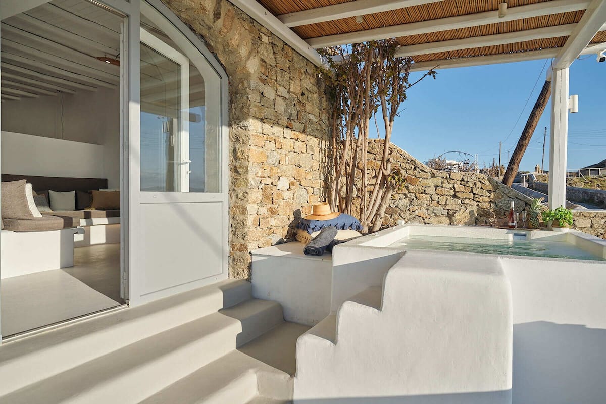 A modern outdoor seating area with a stone wall, a glass door leading inside, and a small pool with a sun lounger.