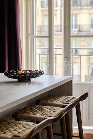 A dining area with a table, wicker chairs, and a window with a view of buildings. - 1.75 Paris La Trêve (Paris)