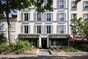 A multi-story building with a central entrance, green awnings, and a café on the right. - 1.75 Paris La Trêve (Paris)