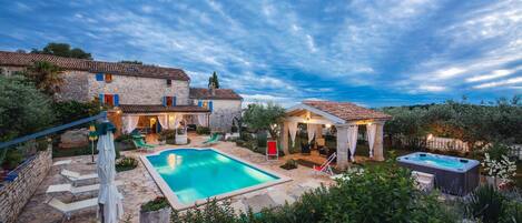Une villa en pierre dotée d’une piscine, d’un espace salon extérieur et d’un jacuzzi.