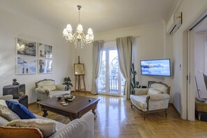 Ein geräumiges Wohnzimmer mit Holzboden, zwei Sesseln, einer Couch, einem Couchtisch und einer Chandelier.