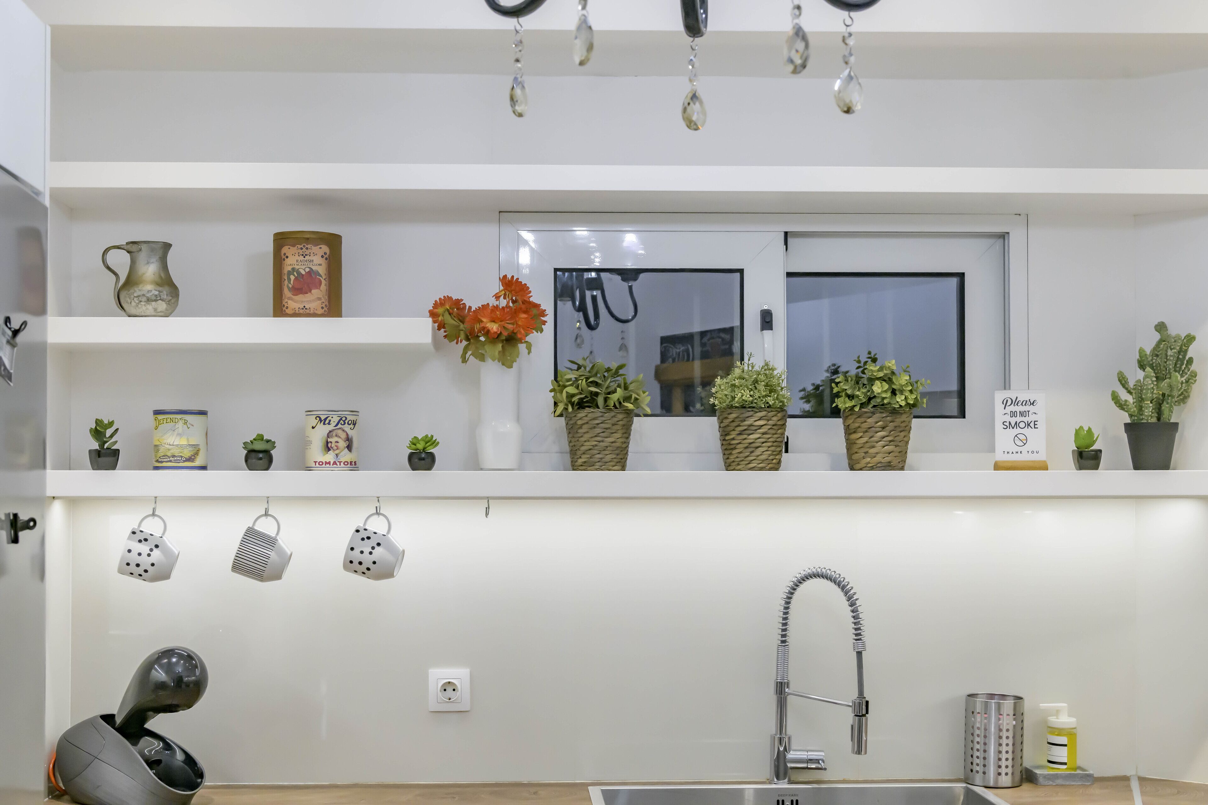 A kitchen with a white countertop, a window, and various kitchen items like a kettle, pots, and potted plants.