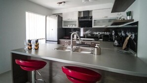 A modern kitchen with a central island, stainless steel appliances, and red bar stools.