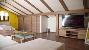 A modern bedroom with a bed, a glass coffee table, a TV, and wooden paneling on the walls.