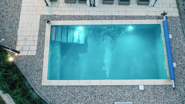 A rectangular swimming pool with a clear blue water surface, surrounded by a pebble border and a tiled deck.