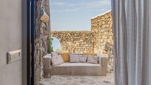 Un espacio de estar al aire libre con pared y piso de piedra, y un sofá con cojines.