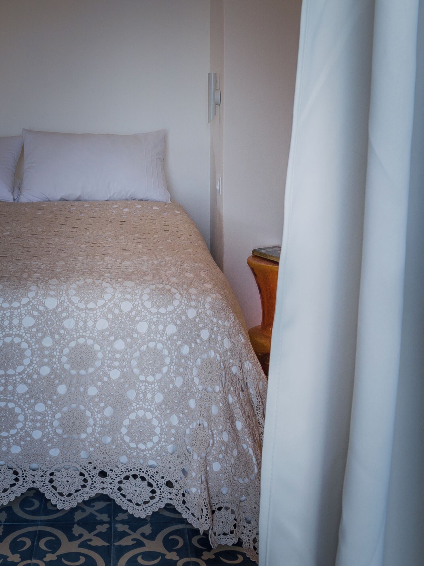 A bed with a patterned bedspread, a bedside table, and a curtain partially drawn.