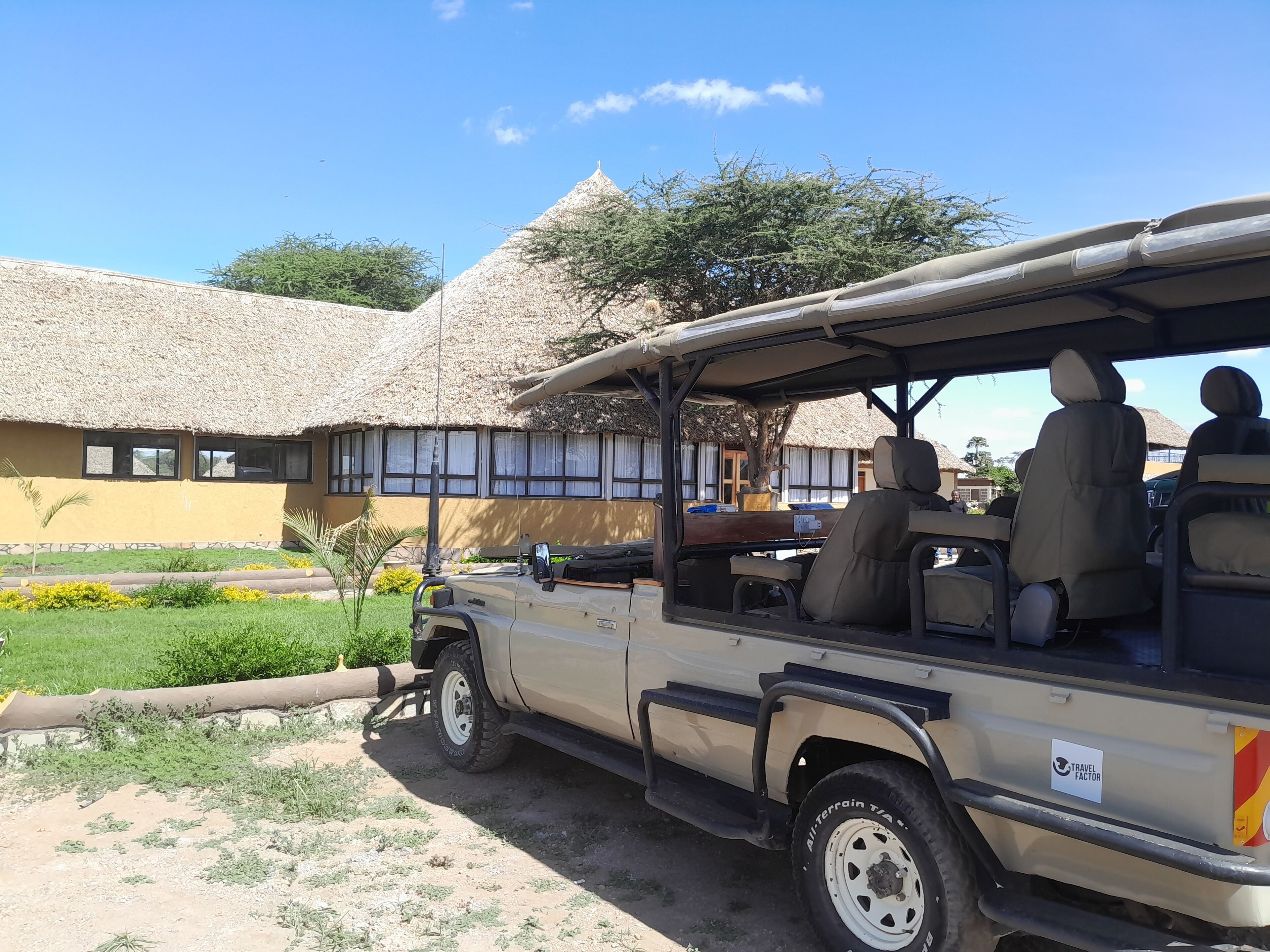 A safari vehicle parked in front of a thatched-roof building with a garden in the foreground.