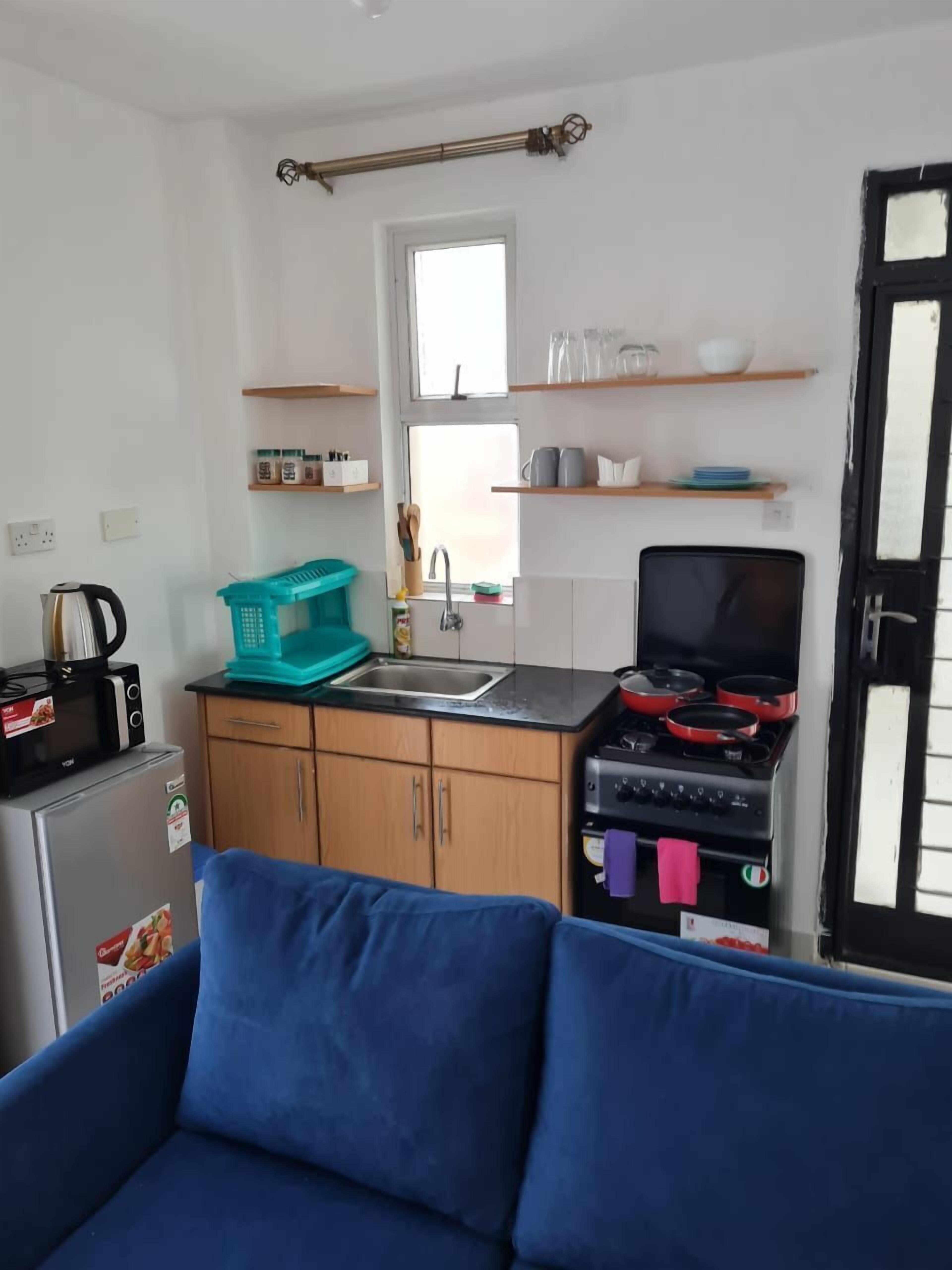 Una cucina compatta con frigorifero, microonde, fornello e lavello. In primo piano, un divano blu.