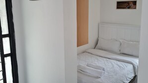 Un dormitori amb un llit, parets blanques, un panell de fusta, una làmpada al sostre, un quadre amb marc i una porta amb estructura negra.