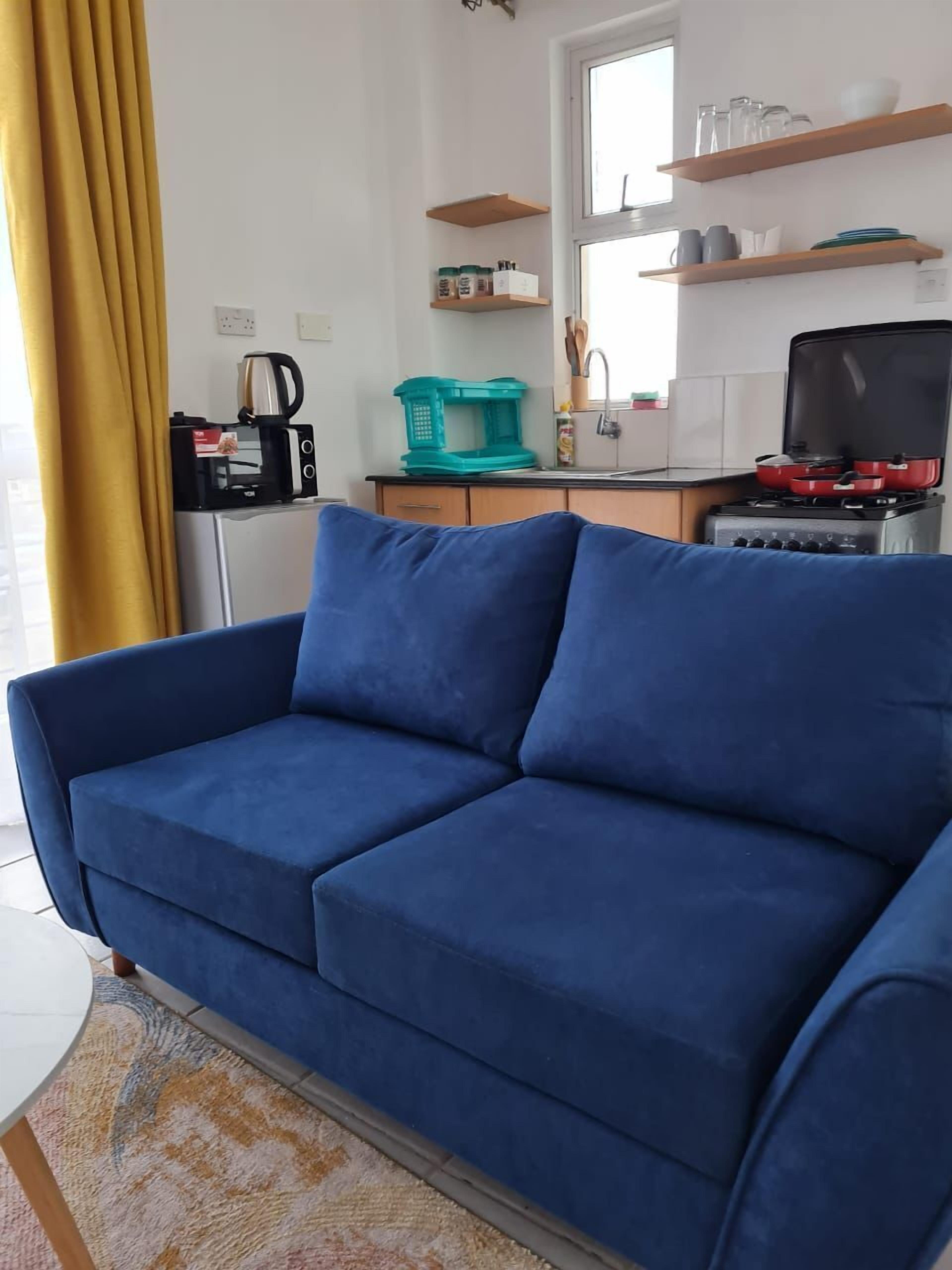 A blue sofa in a modern kitchen with a window, a stove, and kitchen shelves.