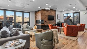 Un salon moderne doté d’une cheminée, de sièges confortables et de grandes fenêtres offrant une vue sur l’extérieur.
