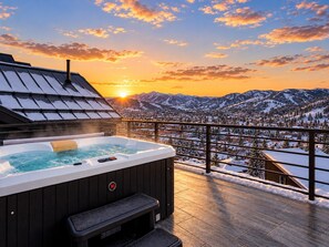 Een hottub op een balkon met uitzicht op besneeuwde bergen en een zonsondergang.