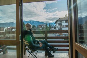 A person seated on a balcony with a view of mountains and buildings. - Banderitsa Apartment 1 (Bansko)