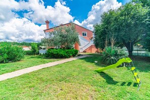 Una casa con fachada roja, una chimenea visible y un jardín con un tobogán verde.