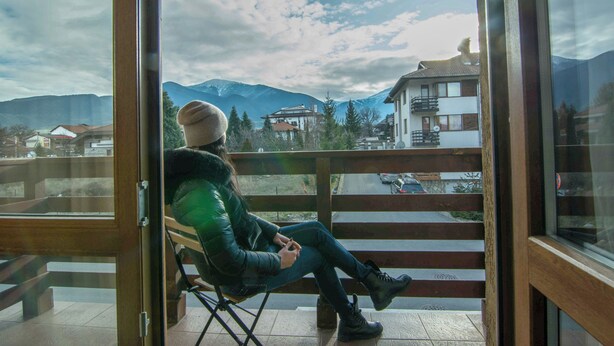 A person seated on a balcony with a view of mountains and buildings. - Banderitsa Apartment 3 (Bansko)