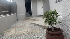A small, enclosed courtyard with a gravel ground, a potted plant, a white door, and a satellite dish on the building. - Kingsworth Inn - Port Elizabeth (Gqeberha (Port Elizabeth))