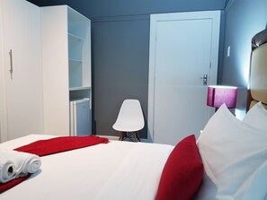 A hotel room with a bed, a wardrobe, a chair, and a lamp. - Kingsworth Inn - Port Elizabeth (Gqeberha (Port Elizabeth))