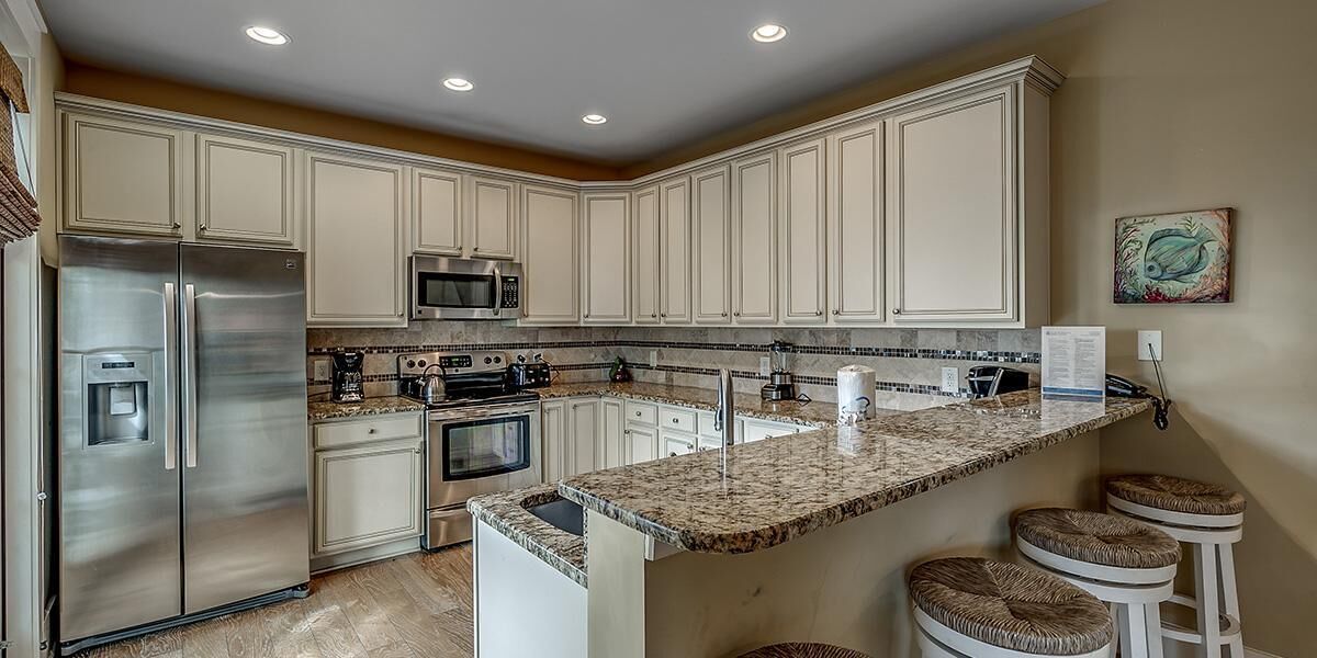 A kitchen with white cabinets, stainless steel appliances, a granite countertop, and a small island with stools.